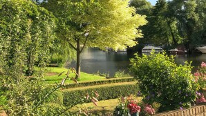 A serene garden with a pond, neatly trimmed hedges, and a variety of potted plants. - 1 bedroom accommodation in Beccles (Beccles)