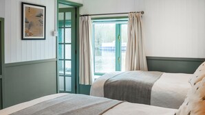 A room with two beds, a window with curtains, a painting on the wall, and a door. - 1 bedroom accommodation in Beccles (Beccles)