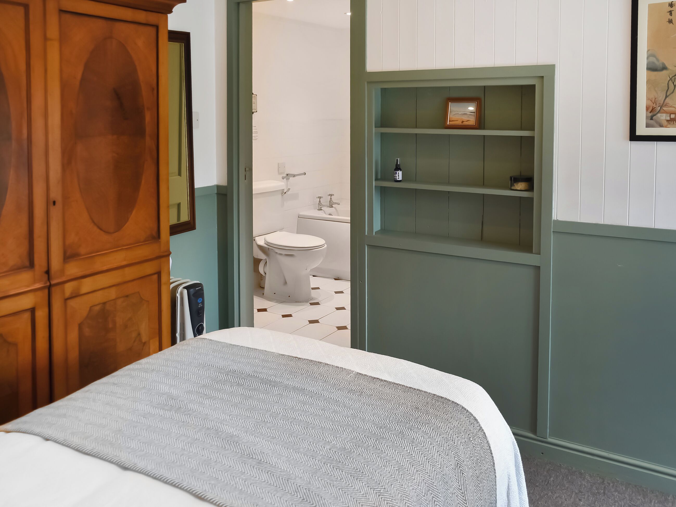 A bedroom with a bed, a wooden wardrobe, a bathroom with a toilet and sink, and a green shelving unit.