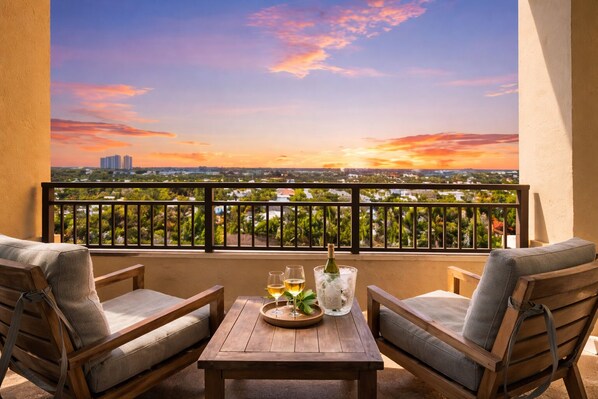A balcony with a wooden table, two cushioned chairs, a bottle of wine, and glasses. - 1 bed condo at the Palm Beach Marriott with Hotel Amenities and views RENOVATED (Riviera Beach)