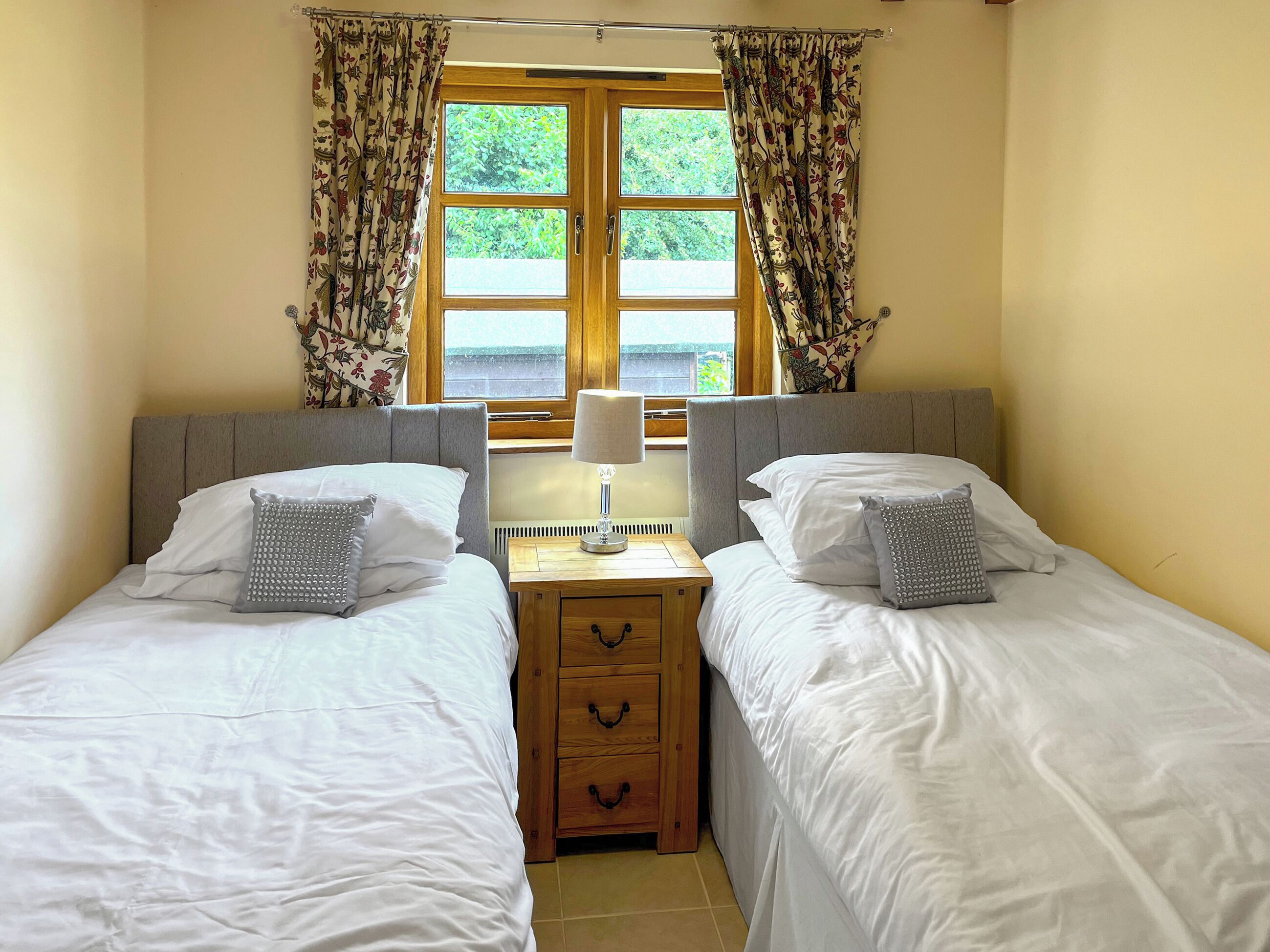 Une chambre double avec deux lits simples, une table de chevet avec une lampe et une fenêtre avec des rideaux.