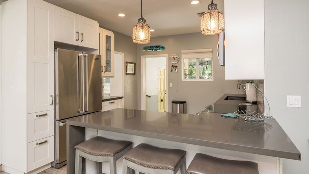 A modern kitchen with white cabinets, a stainless steel refrigerator, a central island with bar stools, pendant lighting, and a view into the adjacent dining area. - ISLAND SANCTUARY KEY WEST - 3 Bedroom / 2 Bathroom with Pool and Parking! (Key West)