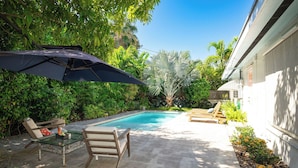 A backyard with a swimming pool, lounge chairs, and a glass table. - ISLAND SANCTUARY KEY WEST - 3 Bedroom / 2 Bathroom with Pool and Parking! (Key West)