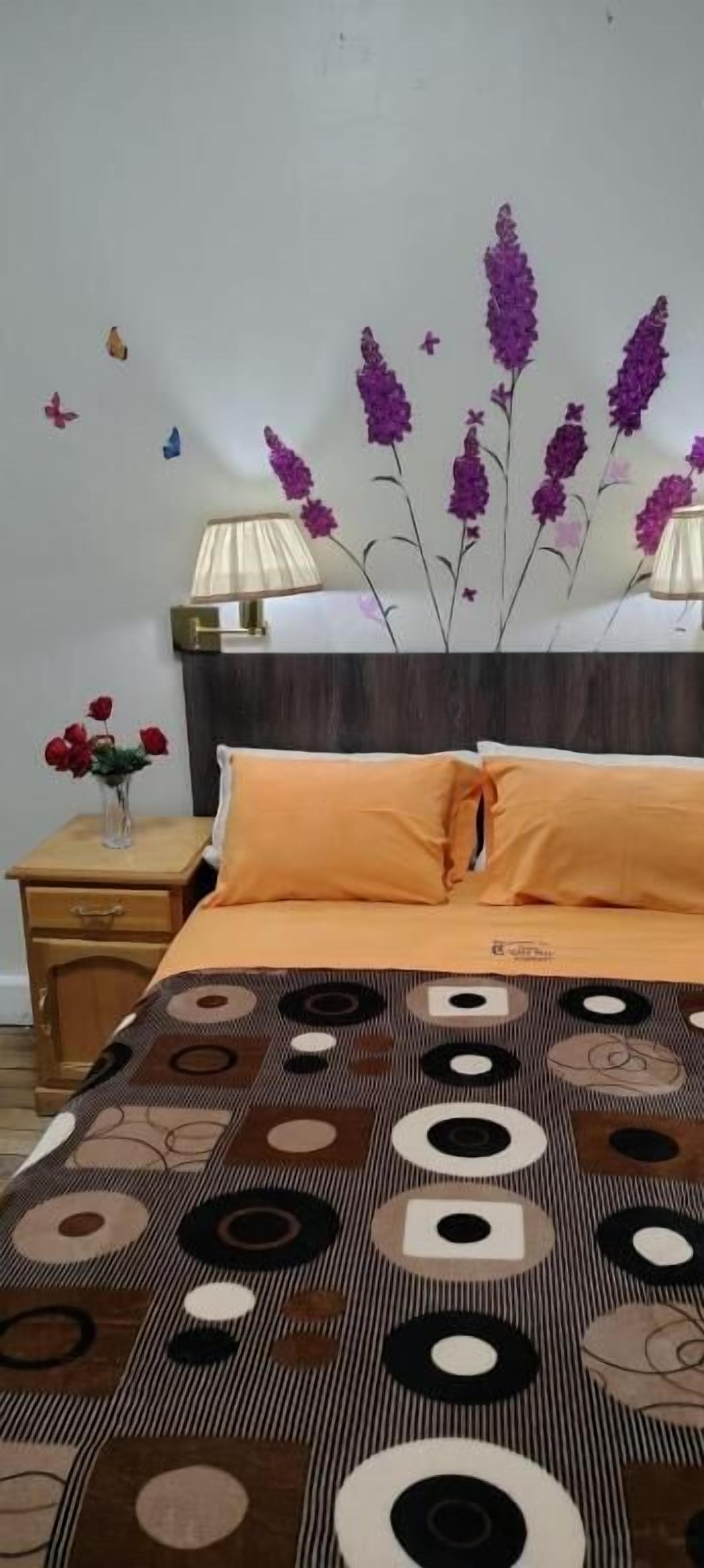 Un dormitorio con cama, mesita de noche, lámpara y un adorno en la pared.