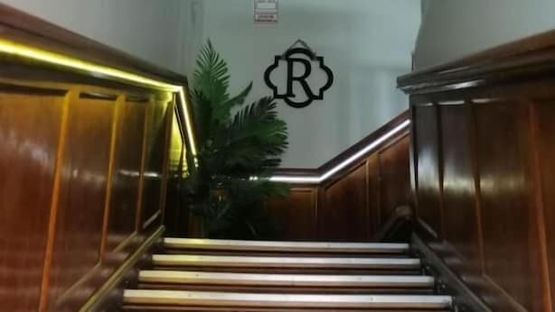 A wooden staircase with a handrail, leading to a landing with a logo. - Posadas Casa Real - Huancayo (Huancayo)