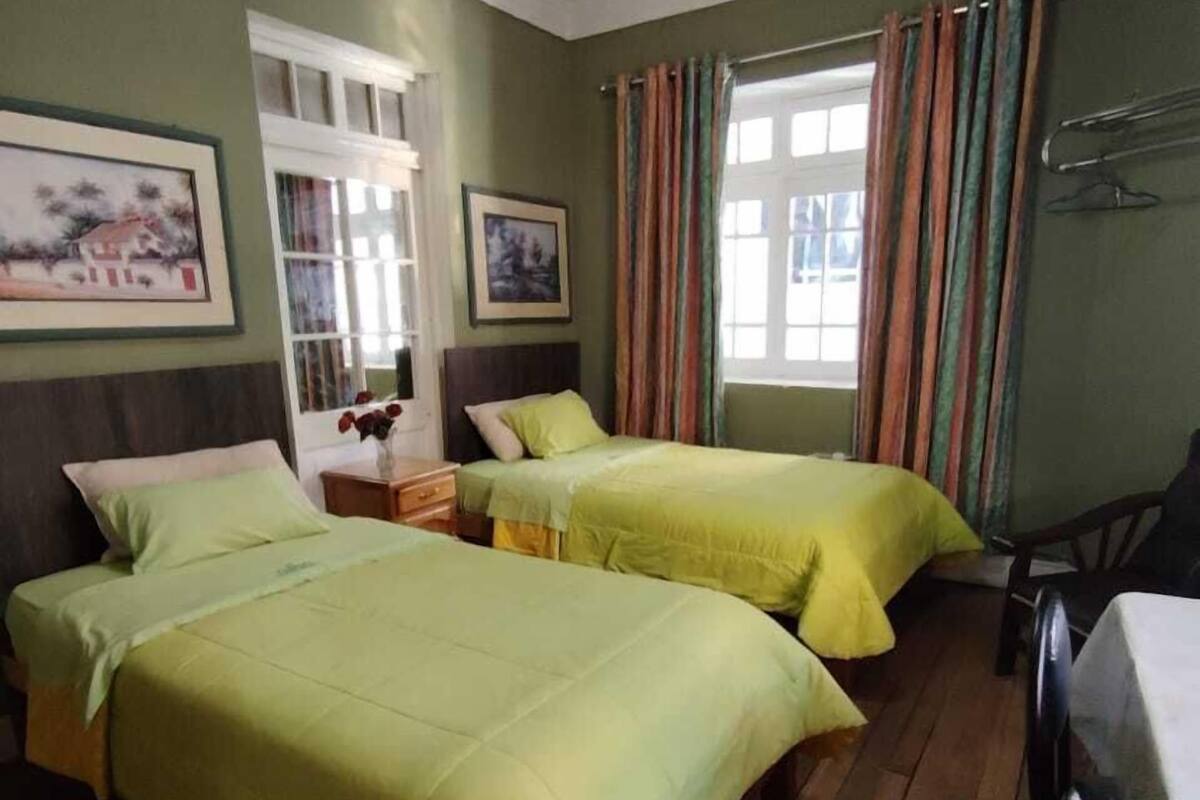 Una habitación con dos camas, piso de madera, una mesa y una silla.