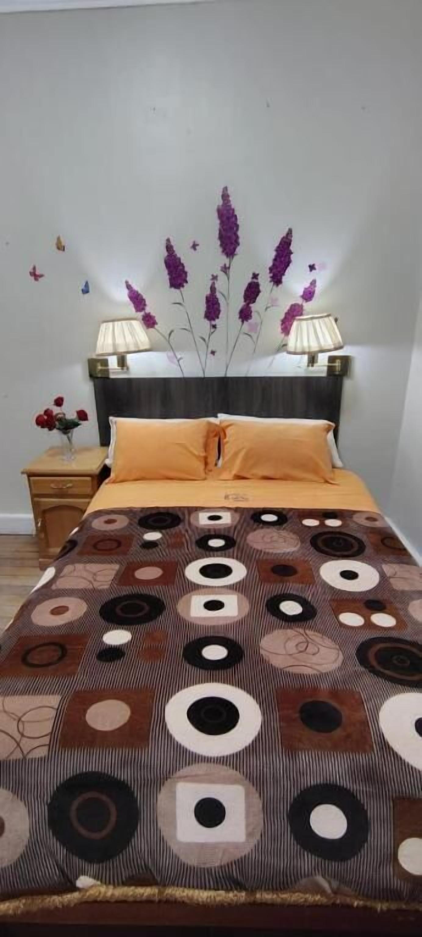 A bedroom with a bed, a nightstand, a lamp, and wall decorations.
