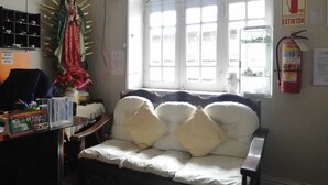 A room with a bed, a desk with a computer, a statue, and a window with blinds. - Posadas Casa Real - Huancayo (Huancayo)