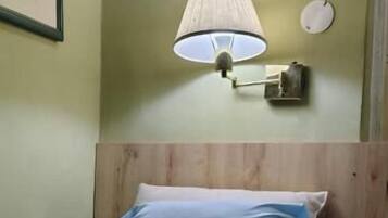 A bed with a patterned blanket, a wall-mounted lamp, and a framed picture.