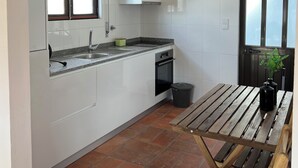 A kitchen with white cabinets, a granite countertop, a window, and a wooden table with a trash bin. - 3-bedroom beach house in enchanting Apúlia with WiFi (Apúlia)
