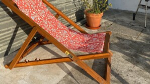 A wooden lounge chair with a red patterned cushion, a potted plant, and a barbecue grill against a brick wall. - 3-bedroom beach house in enchanting Apúlia with WiFi (Apúlia)