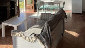 A spacious living area with a wooden ceiling, a stone fireplace, a dining table with chairs, and a refrigerator. - 3-bedroom beach house in enchanting Apúlia with WiFi (Apúlia)