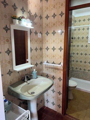 Un baño con baldosas estampadas, un lavamanos con espejo, un inodoro y una zona de ducha.