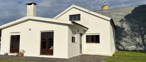 Une maison blanche à deux étages, dotée d’une cheminée, d’une porte d’entrée et de deux fenêtres.