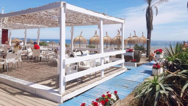 A covered outdoor seating area with white chairs and tables, a pool, and palm trees. - Three Bedroom Townhouse 100 meters from the Beach! (Playa del Sol Villacana)