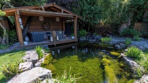 A wooden deck with outdoor furniture, a pond, and surrounding greenery. - Couple's Oasis at Horner Park, Welch Homes & Hospitality, pet friendly property. (Saanich)