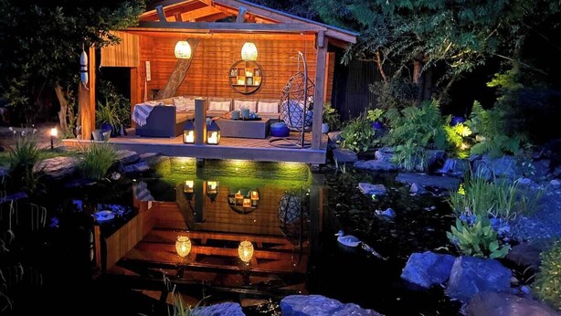A wooden cabin with a pond, seating area, and lanterns. - Couple's Oasis at Horner Park, Welch Homes & Hospitality, pet friendly property. (Saanich)