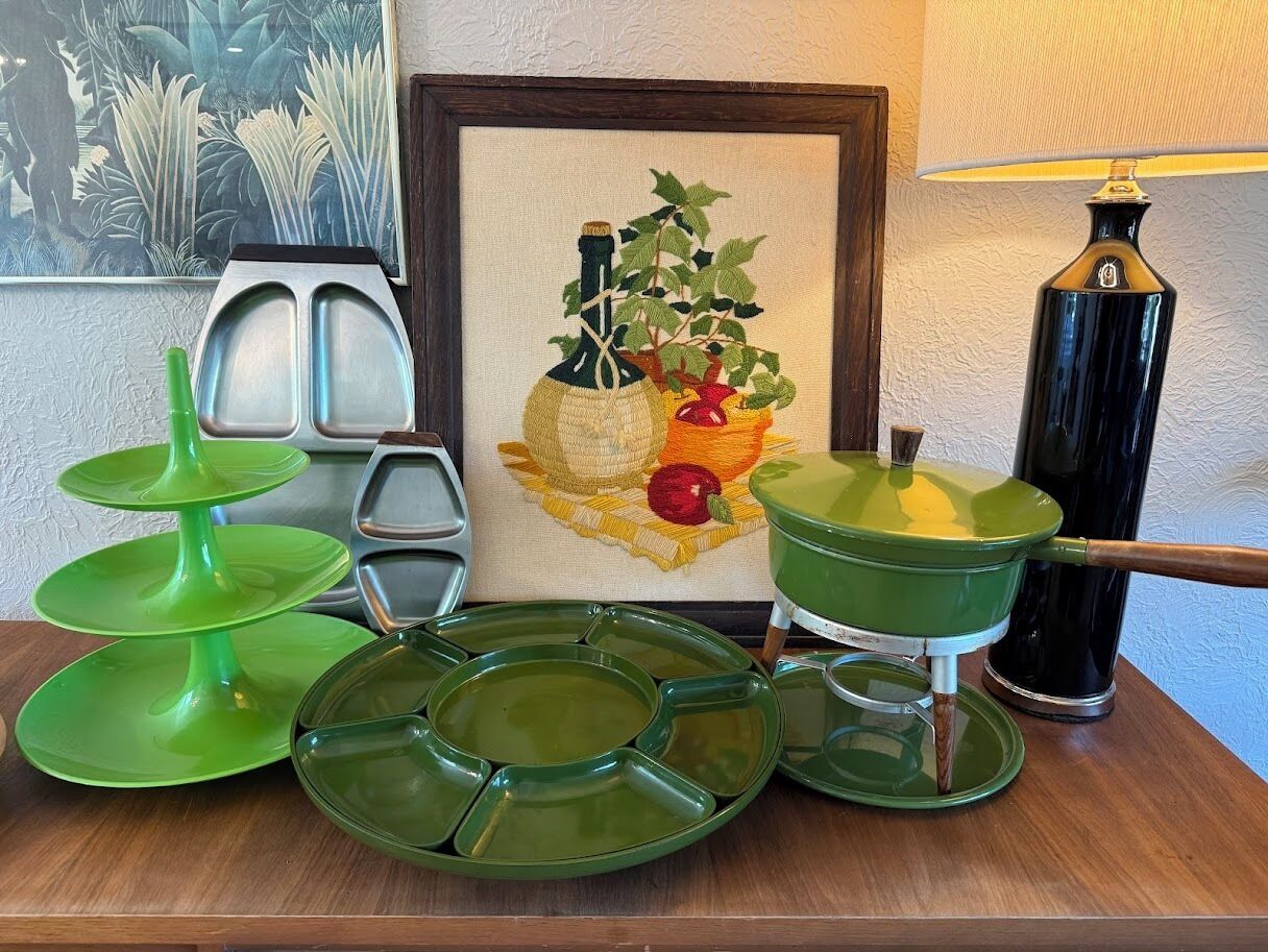 Una mesa con vajilla verde, una olla verde, un cuadro enmarcado y una lámpara.