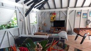 A cozy living area with a sofa, a coffee table, and a foosball table. There are decorative plants and a TV in the background. - Spacious Beagwada villa ideal for vacations with family or friends. (Saint-François)