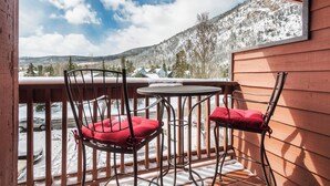 Varanda com duas cadeiras e uma mesa, com vista para uma paisagem montanhosa coberta de neve.