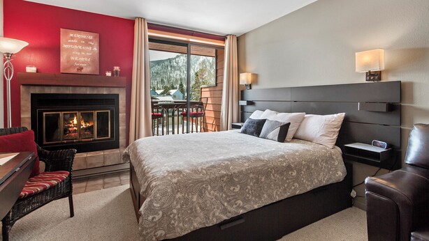 Quarto de hotel com uma cama grande, lareira, área de jantar com mesa e cadeiras, e vista para as montanhas.
