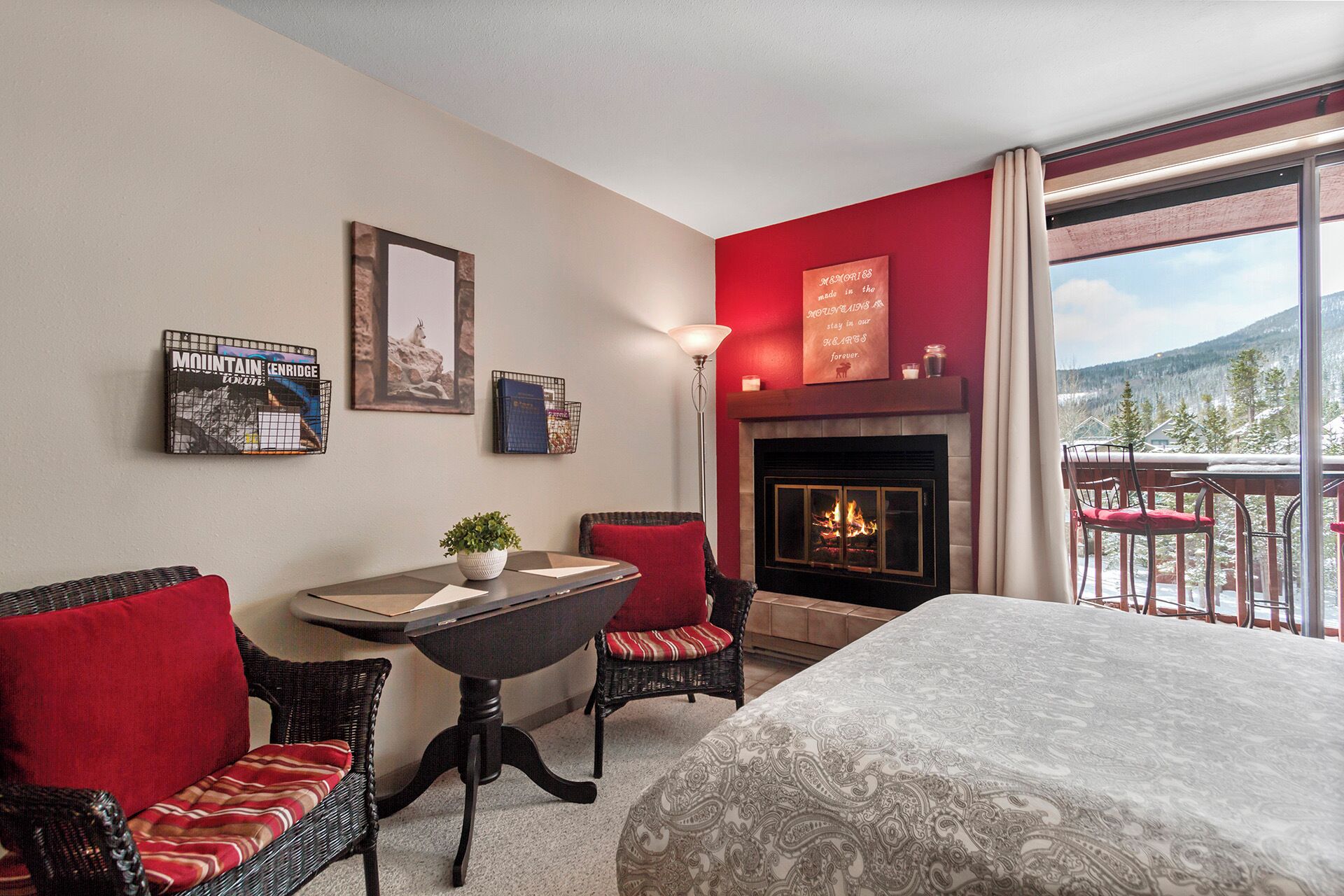 Une chambre d’hôtel avec une cheminée, un balcon offrant une vue sur les montagnes enneigées et un coin repas avec des meubles en osier.