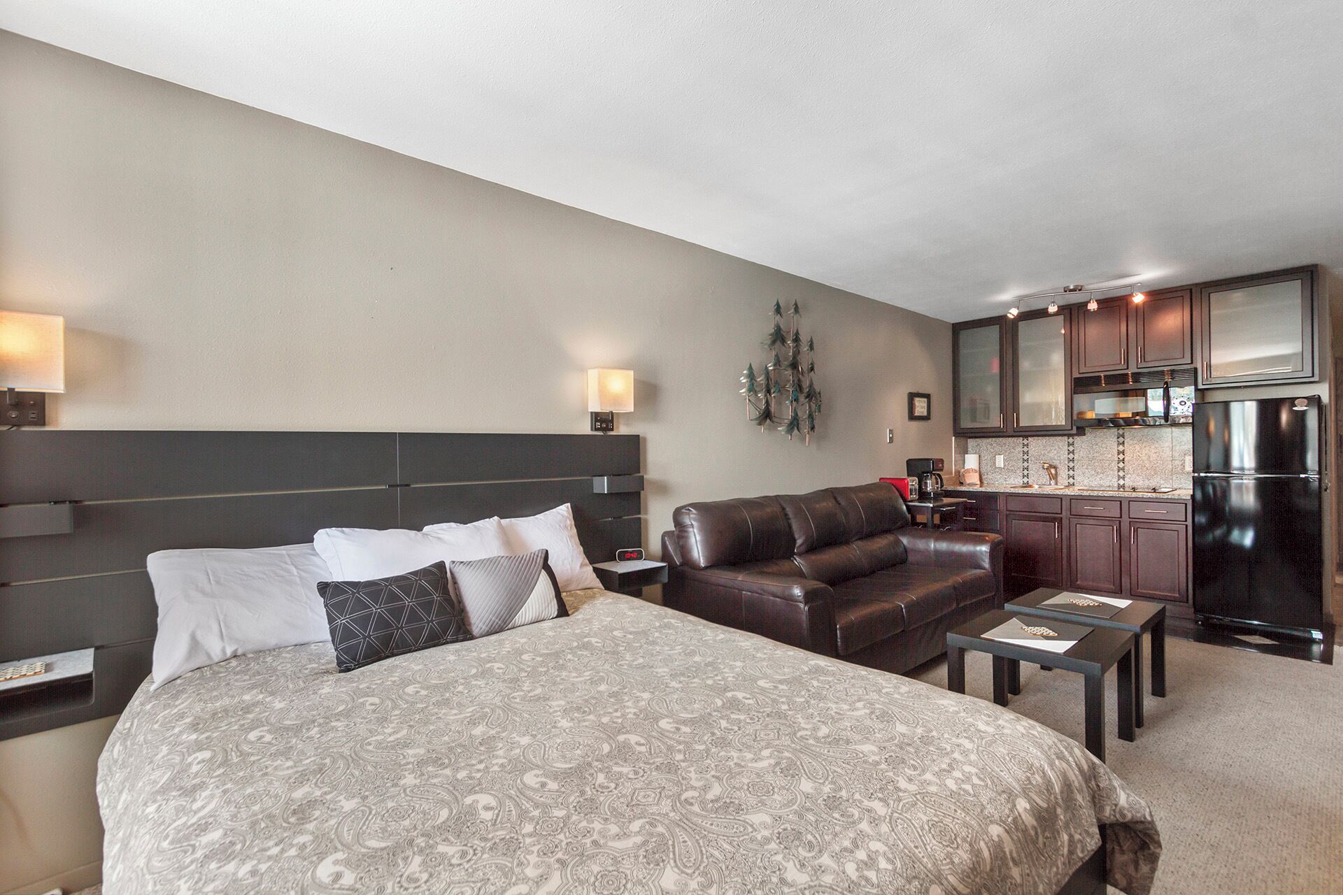Una habitación de hotel con una cama grande, un sofá de cuero, una mesita y una kitchenette.