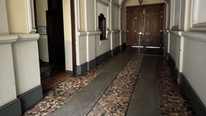 A hallway with a tiled floor, arched ceilings, and a wooden door at the end. - Massena street (Torino)