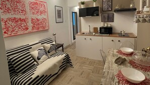 A modern living room with a sofa, a dining table with a glass top, and a kitchen area with a microwave and a coffee machine. - Massena street (Torino)