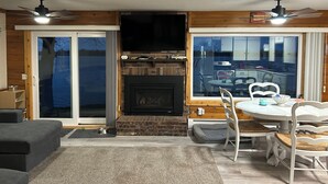 A cozy living room with a fireplace, a dining area with a table and chairs, and a large window offering a view of the outdoors. - Finch House on Lake Osakis: Charming 2-bedroom cabin (Osakis)