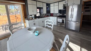 A kitchen with white cabinets, a stainless steel refrigerator, a dining table with chairs, and a ceiling fan. - Finch House on Lake Osakis: Charming 2-bedroom cabin (Osakis)