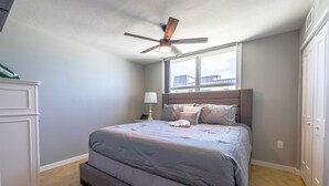 A bedroom with a bed, a ceiling fan, a window, and a nightstand.