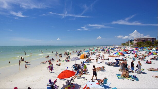 A crowded beach with people sunbathing and swimming.