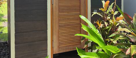 A wooden structure with a door, surrounded by plants and gravel.