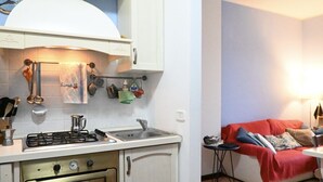 A compact kitchen with a gas stove, oven, and a sink. There is a small table and a couch in the adjacent living area. - S346 – Sirolo, three-room apartment in a residential area (Sirolo)