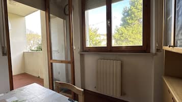 A room with a table, a radiator, a window with blinds, and a door leading to an outdoor area.