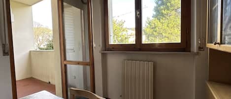 A room with a table, a radiator, a window with blinds, and a door leading to an outdoor area.