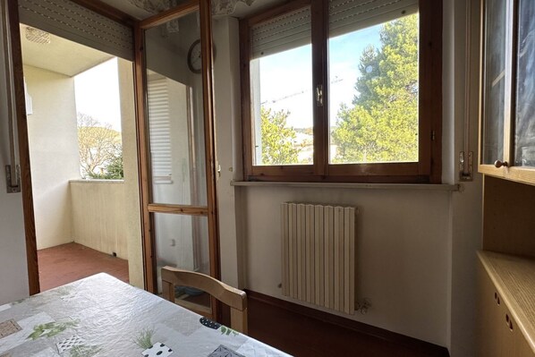 Una habitación con una mesa, un radiador, una ventana con persianas y una puerta que da a un espacio exterior.