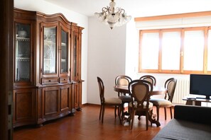 Un comedor con un armario de madera, una araña, una mesa de comedor con sillas y un televisor.