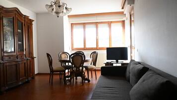 Una sala de estar con sofá, mesa de comedor, sillas, candelabro y televisor.