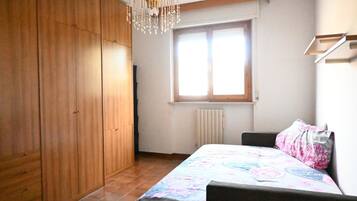A bedroom with a bed, a wardrobe, a radiator, and a window.