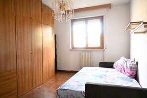 Un dormitorio con cama, armario, radiador y ventana.
