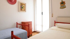 Quarto com duas camas, um guarda-roupa, uma porta e um chapéu fixado na parede.