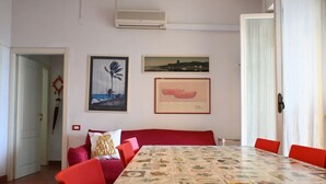 Uma área de refeições com uma mesa posta para quatro pessoas, cadeiras vermelhas, um sofá vermelho com almofada e duas fotos emolduradas na parede.