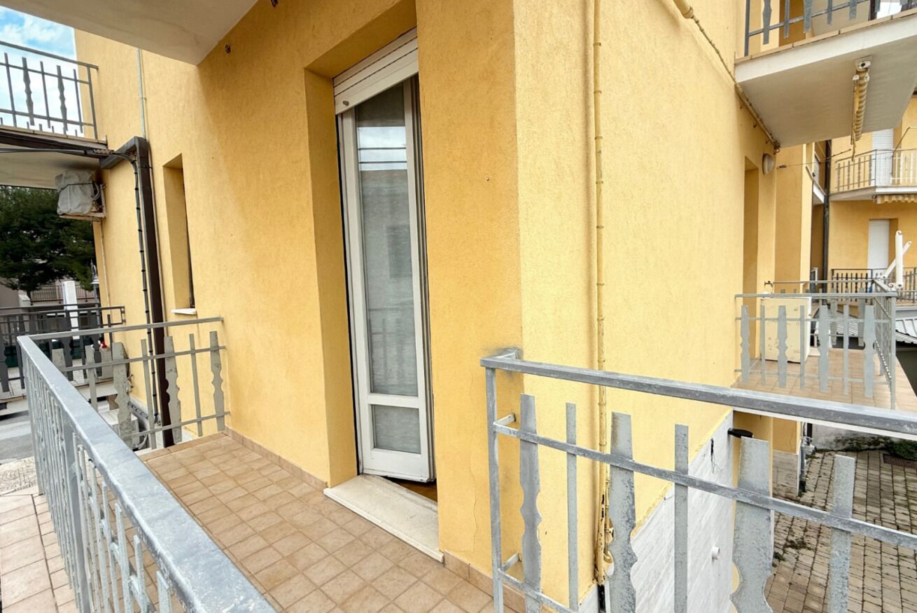 Un edificio giallo con ringhiera in metallo, porta scorrevole in vetro e pavimento piastrellato.