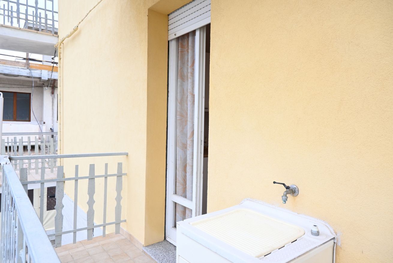 Ein kleiner Balkon mit weißer Reling, ein Fenster mit Vorhang und ein weißer Heizkörper.