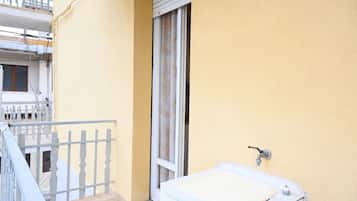 Ein kleiner Balkon mit weißer Reling, ein Fenster mit Vorhang und ein weißer Heizkörper.