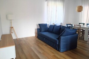Una sala de estar moderna con un sofá azul, piso de madera, una mesa blanca y una lámpara.