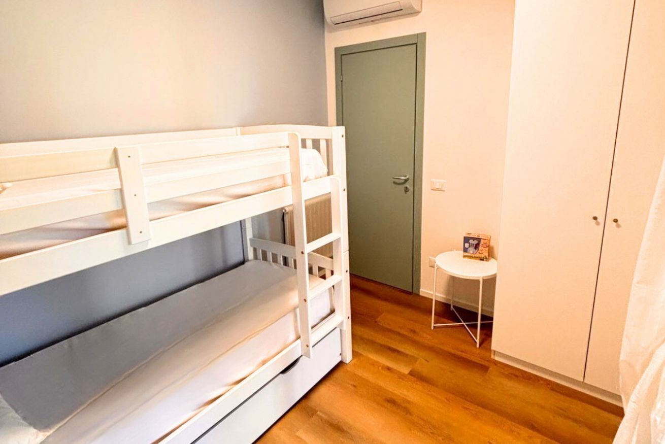 En våningssäng i ett rum med en dörr, ett litet bord och en garderob.