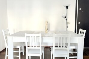 Un coin repas avec une table et des chaises blanches, un vase posé sur la table et une lampe.